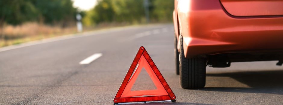 Red car with triangle road sign placed beside it signaling caution